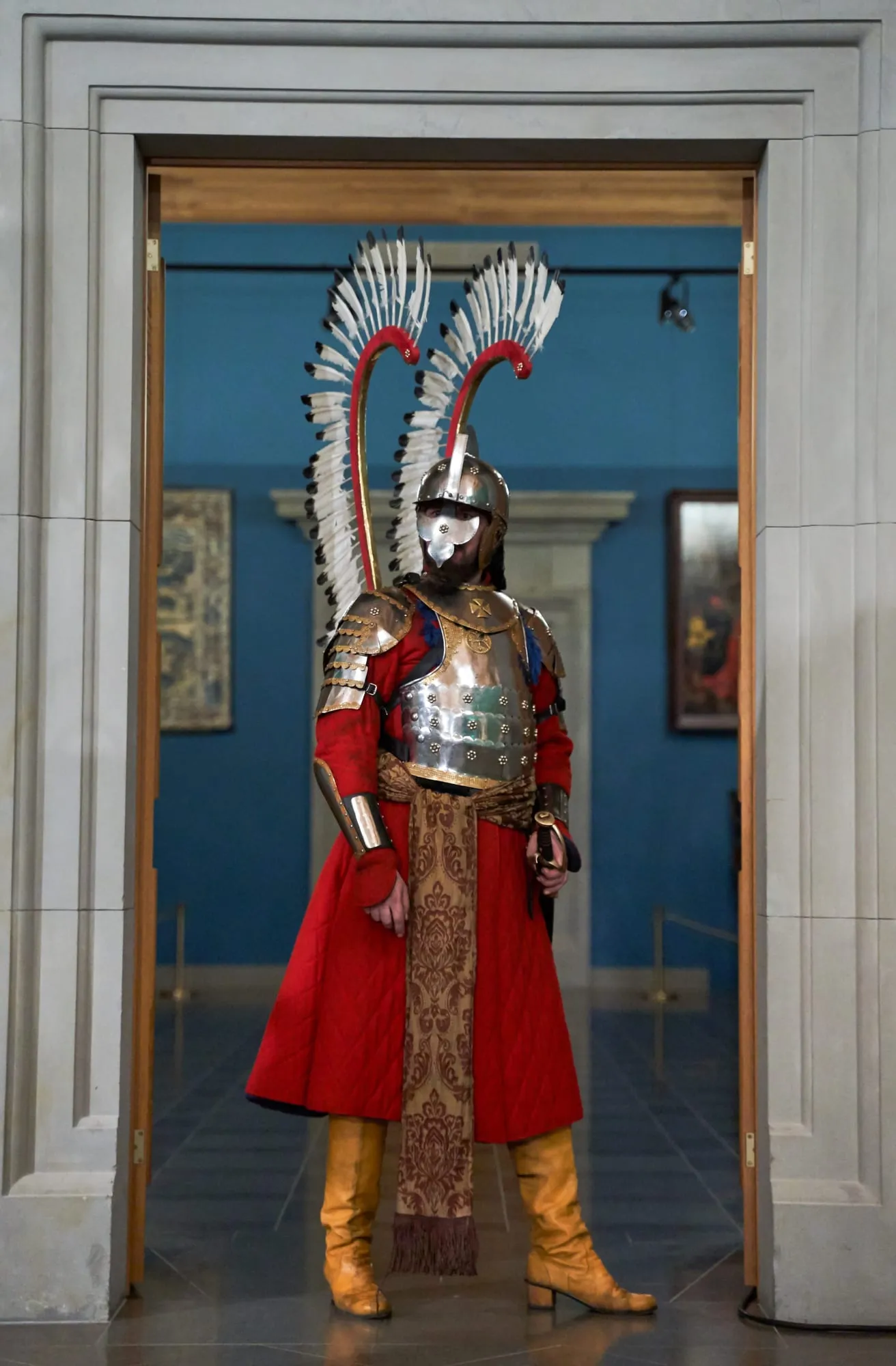 Sparnuotasis husaras šarvais ir sparnais stovi menėje prie durų