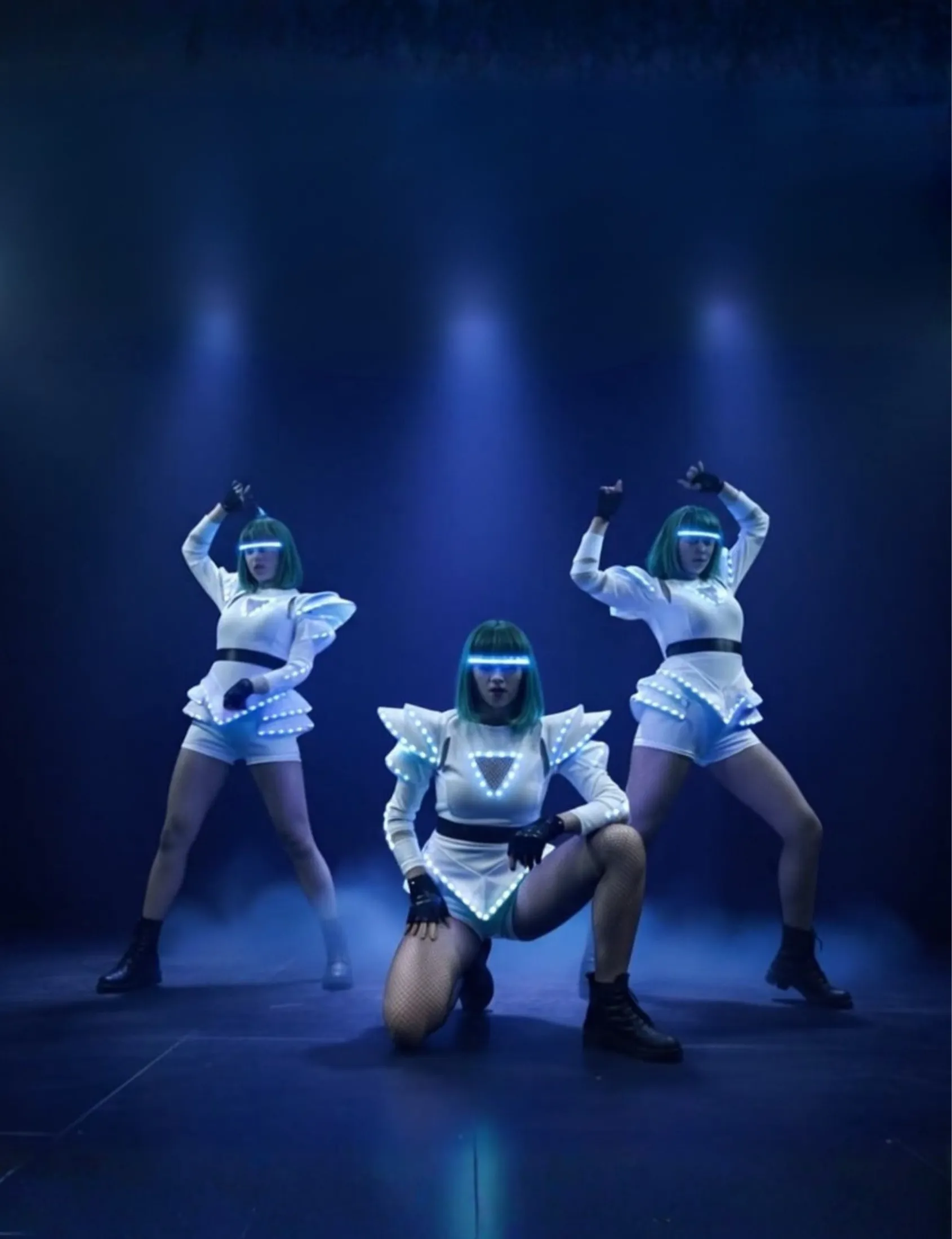 Trys šokėjos su LED kostiumais atlieka choreografiją scenoje