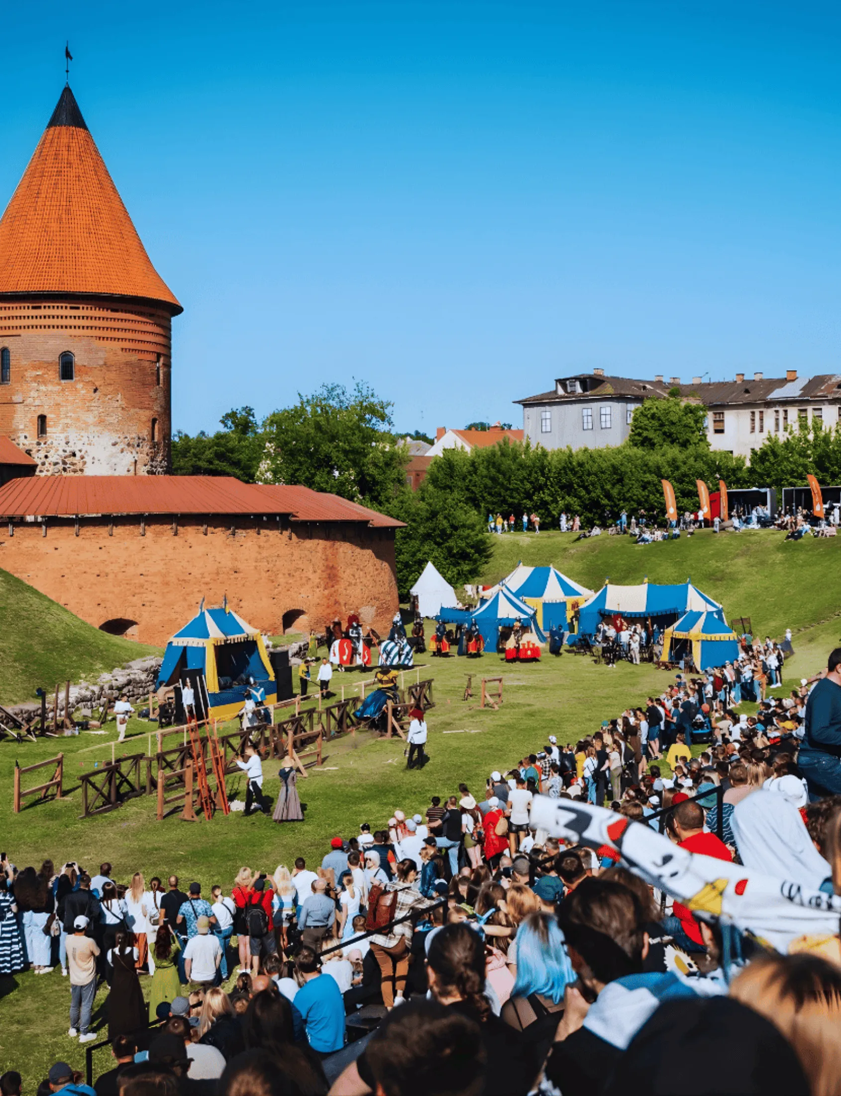 A knights' tournament watched by a huge crowd beside a medieval castle